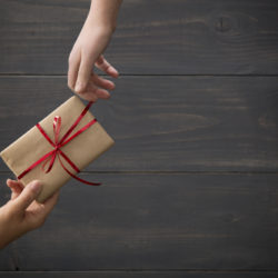 hands passing a gift wrapped in brown paper with a red bow.